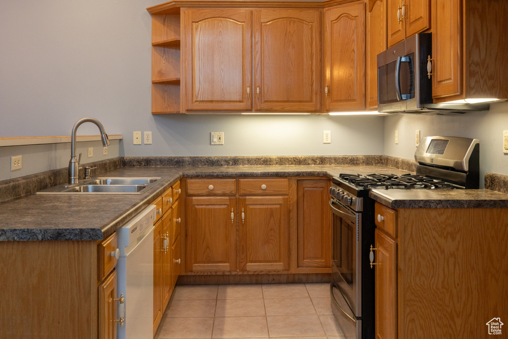 Kitchen featuring appliances with stainless steel finishes, a sink, dark countertops, light tile patterned flooring, and open shelves