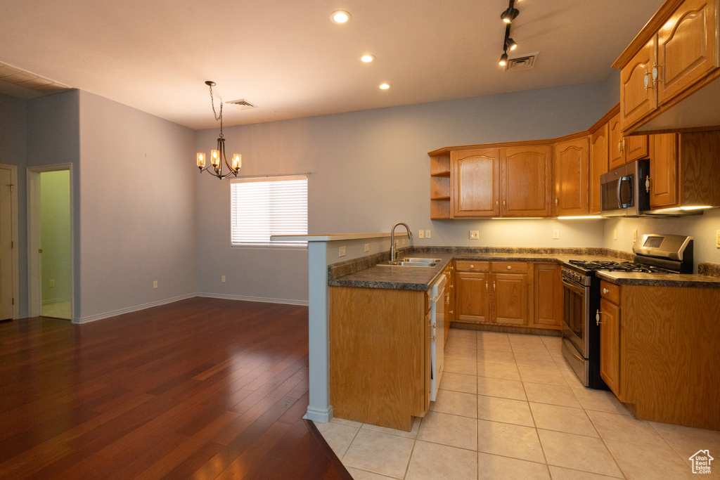 Kitchen featuring appliances with stainless steel finishes, a sink, brown cabinetry, a peninsula, and a chandelier
