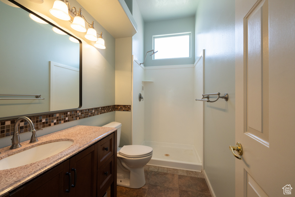 Full bathroom featuring a shower stall, toilet, vanity, and tasteful backsplash