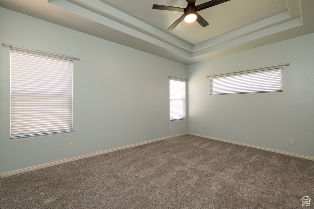 Carpeted spare room featuring a ceiling fan, a tray ceiling, and baseboards