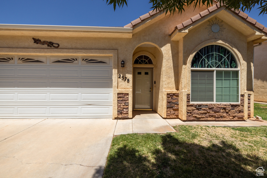 Property entrance featuring driveway, stucco siding, an attached garage, and stone siding