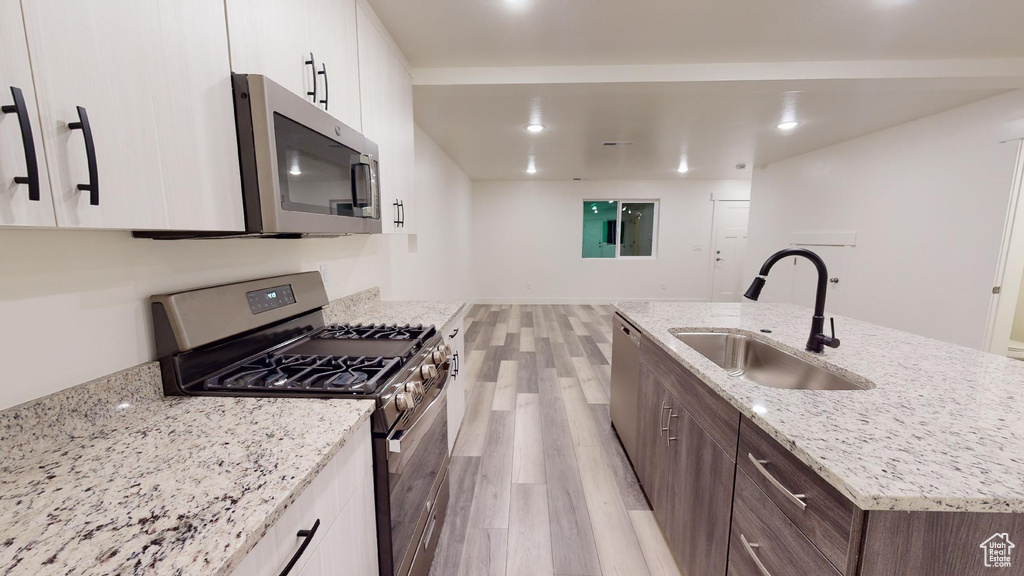 Kitchen with appliances with stainless steel finishes, a sink, light wood finished floors, white cabinetry, and a kitchen island with sink