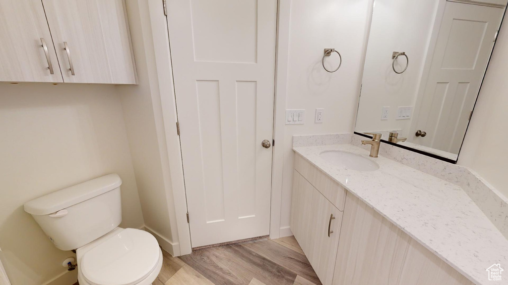 Half bath with toilet, wood finished floors, vanity, and baseboards