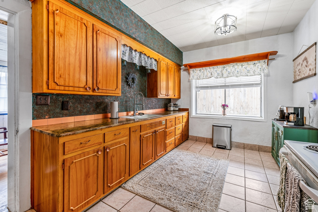 Kitchen featuring a sink, white range with electric stovetop, brown cabinets, backsplash, and dark countertops