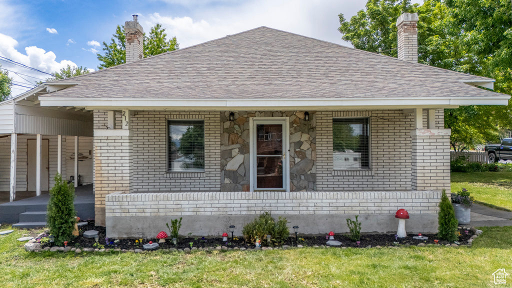 Bungalow with brick siding, a chimney, roof with shingles, a front yard, and a porch