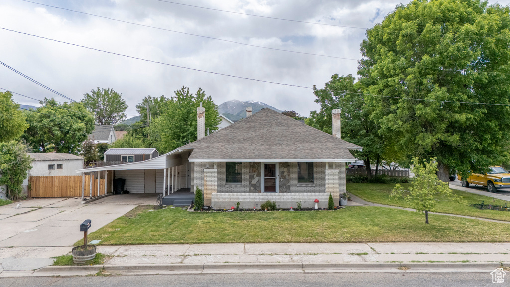 Bungalow featuring brick siding, driveway, roof with shingles, a chimney, and an attached carport