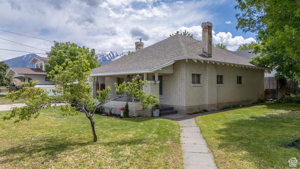 View of front of home with a chimney, a front yard, covered porch, and roof with shingles