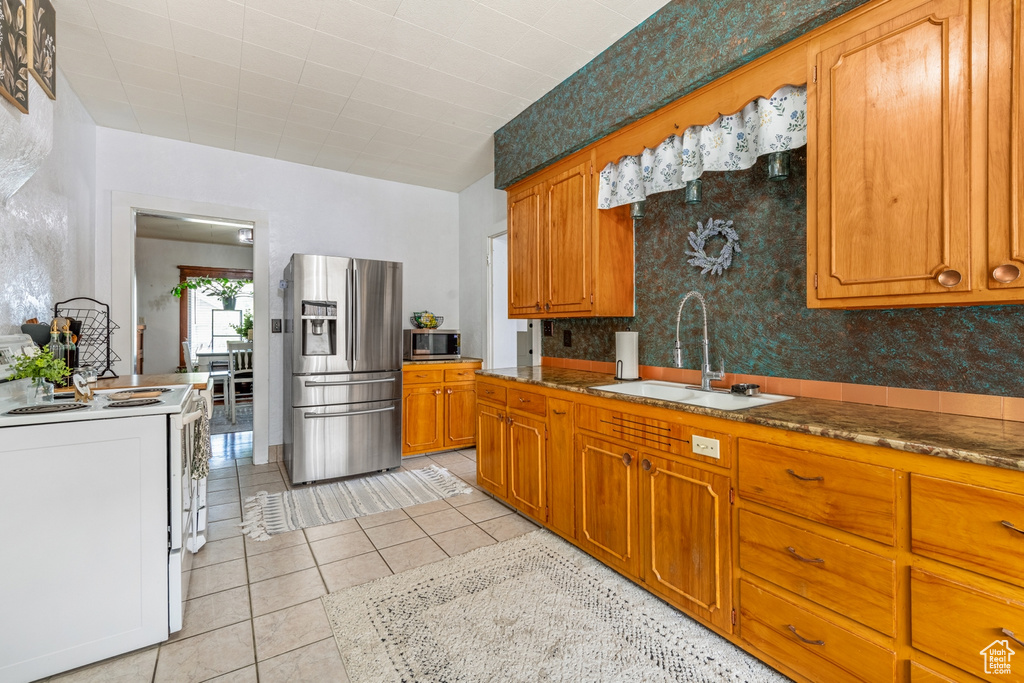Kitchen featuring appliances with stainless steel finishes, a sink, brown cabinets, light tile patterned flooring, and wallpapered walls