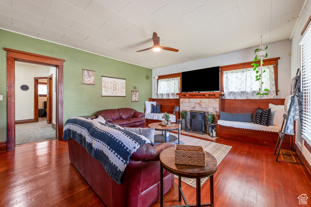 Living room featuring a tile fireplace, hardwood / wood-style floors, a ceiling fan, and baseboards