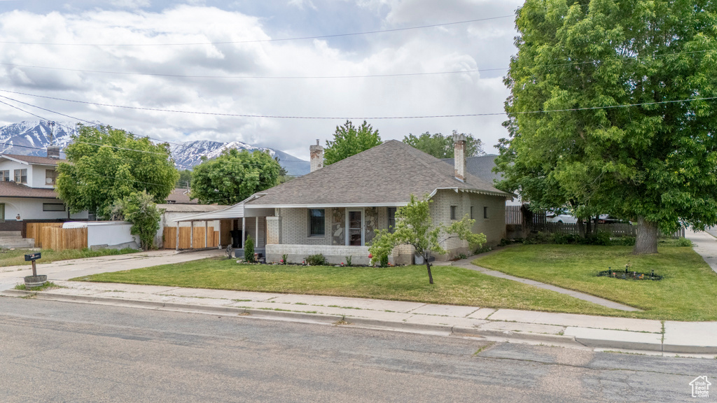 View of front of house featuring brick siding, concrete driveway, roof with shingles, a chimney, and a mountain view