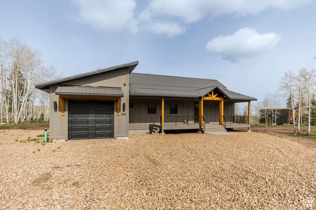 View of front facade with board and batten siding, an attached garage, a porch, and gravel driveway
