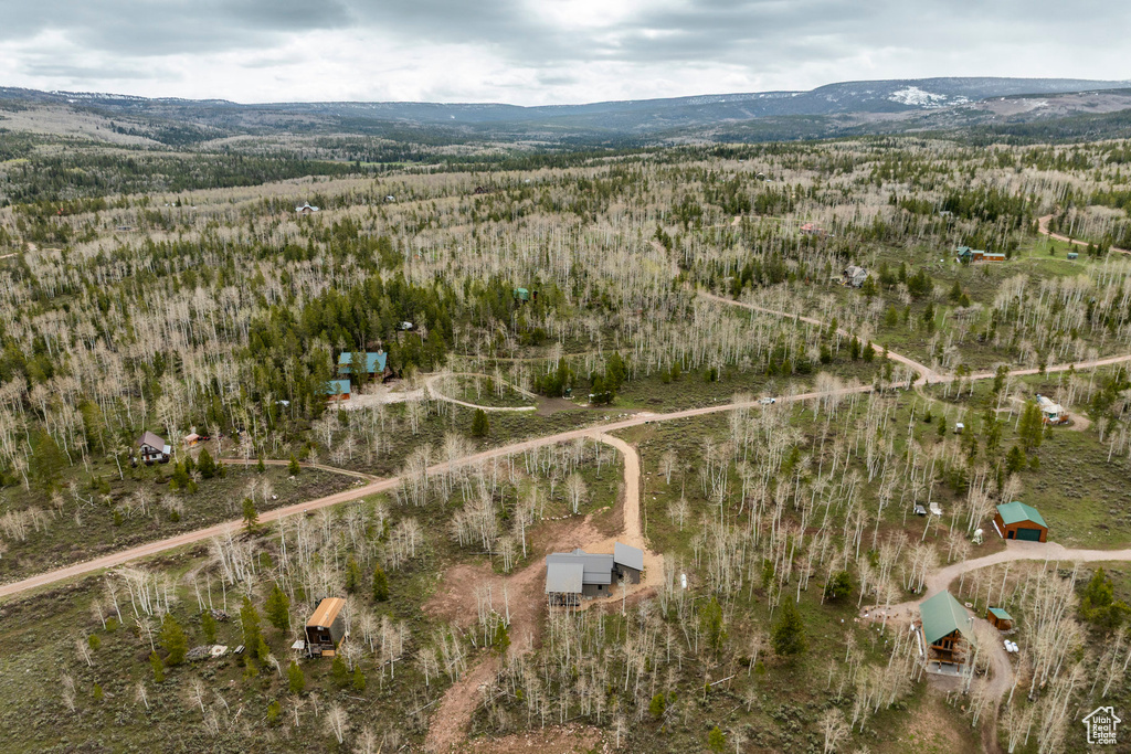 Aerial view of property's location featuring a forest and a mountainous background