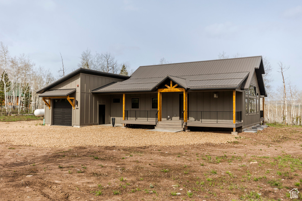 View of front of house with covered porch, an attached garage, dirt driveway, board and batten siding, and metal roof