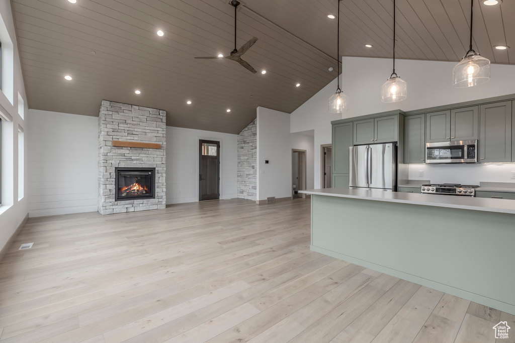 Kitchen featuring appliances with stainless steel finishes, high vaulted ceiling, light countertops, a ceiling fan, and a stone fireplace