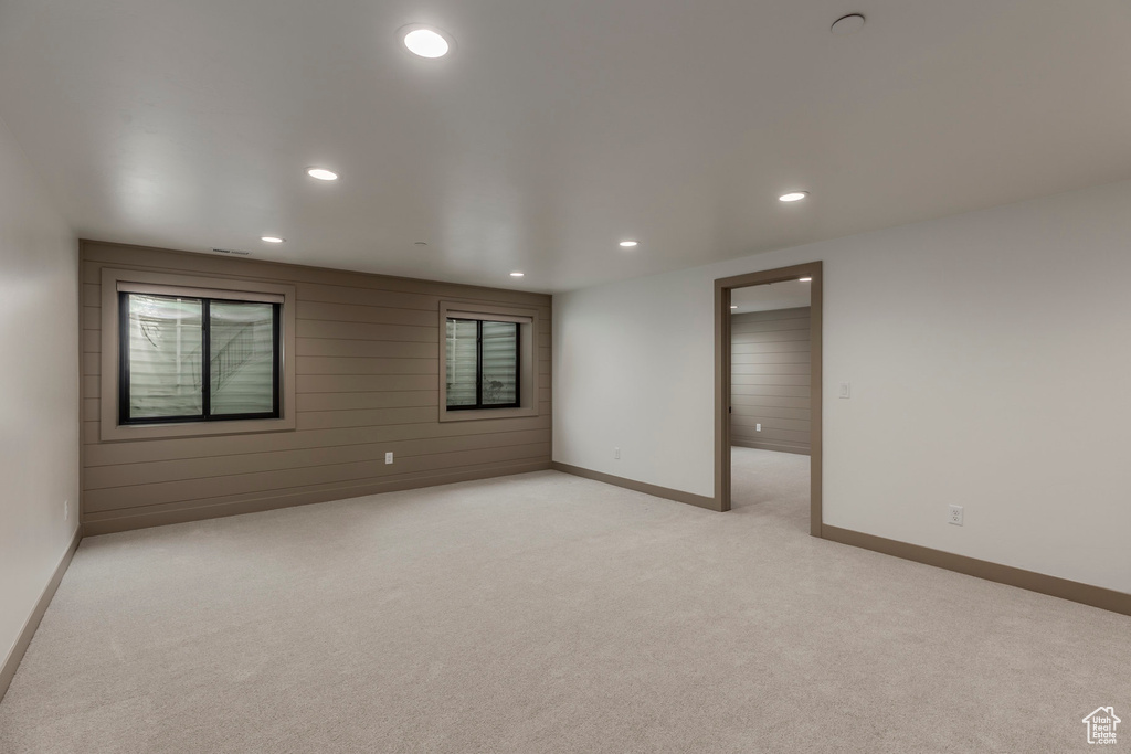 Empty room featuring recessed lighting, light colored carpet, baseboards, and wood walls