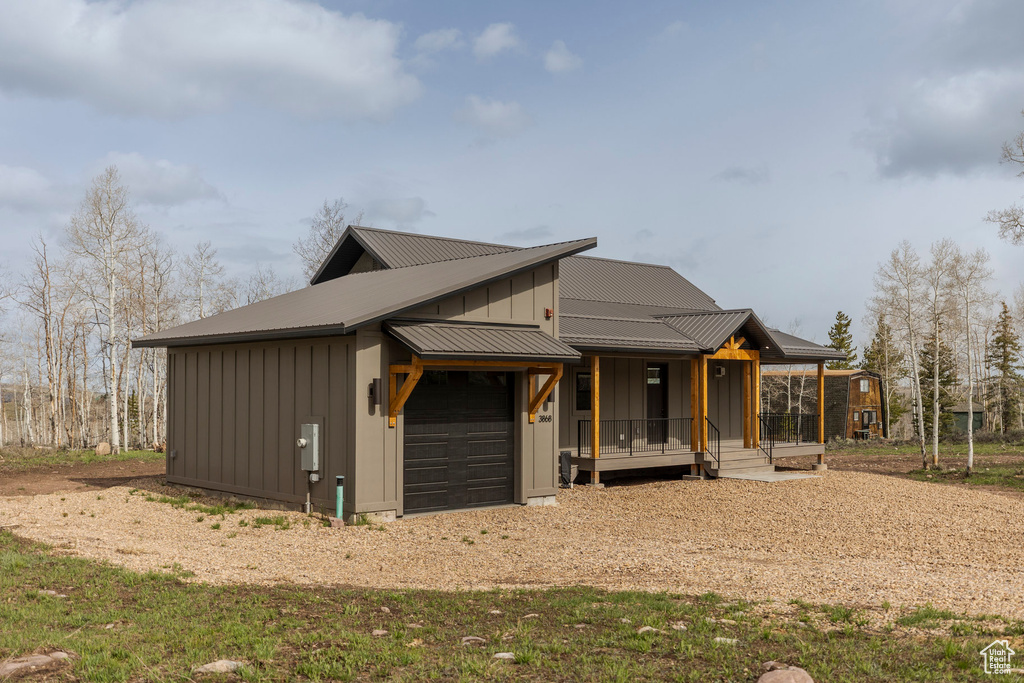 View of front facade with board and batten siding, a garage, metal roof, dirt driveway, and a porch
