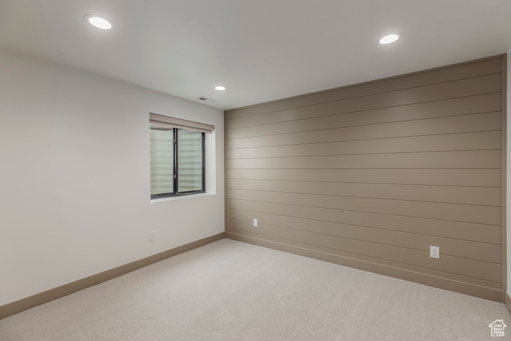 Unfurnished room with light colored carpet, recessed lighting, baseboards, and wood walls