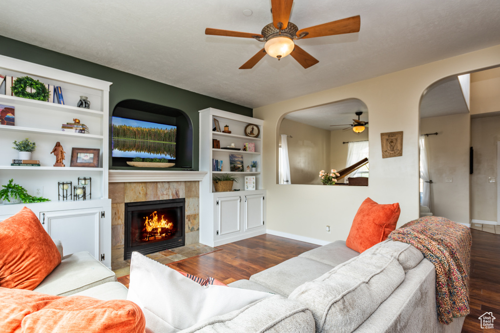 Living area featuring a ceiling fan, arched walkways, wood finished floors, and a tiled fireplace