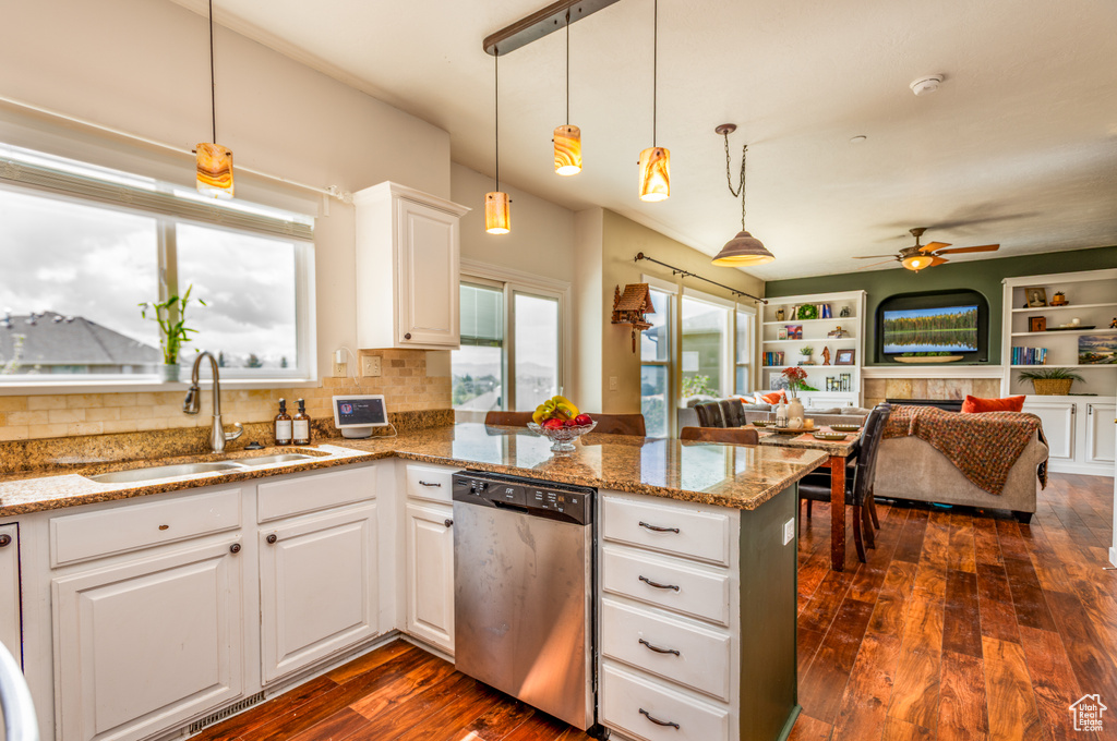 Kitchen with stainless steel dishwasher, a sink, a peninsula, white cabinets, and dark wood-style flooring