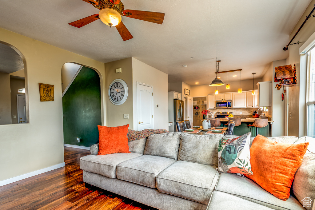 Living room with dark wood finished floors, a ceiling fan, arched walkways, and baseboards