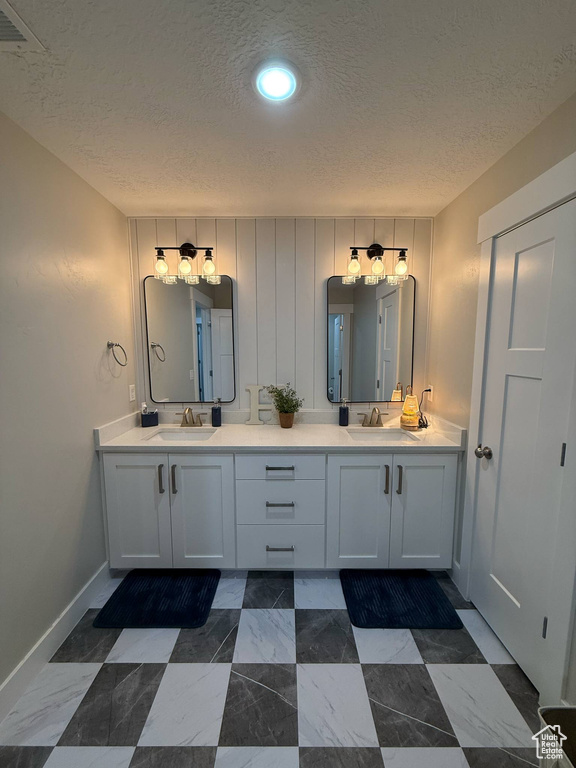 Bathroom featuring a textured ceiling, double vanity, and baseboards