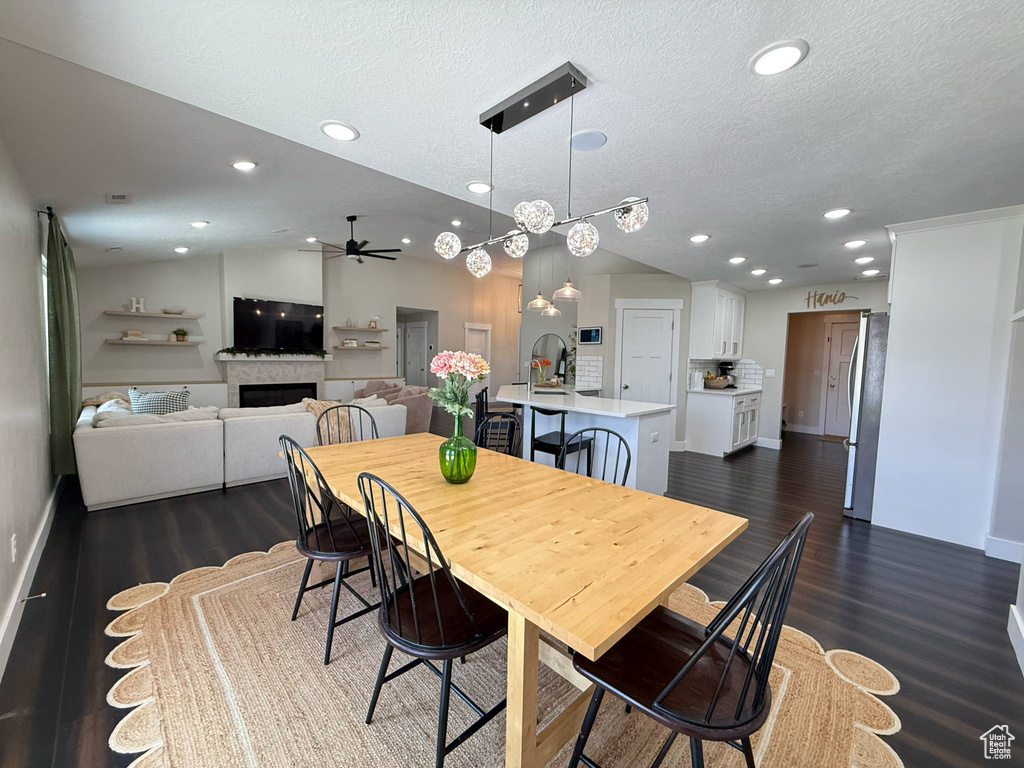 Dining area with a ceiling fan, a fireplace, dark wood-type flooring, a textured ceiling, and baseboards
