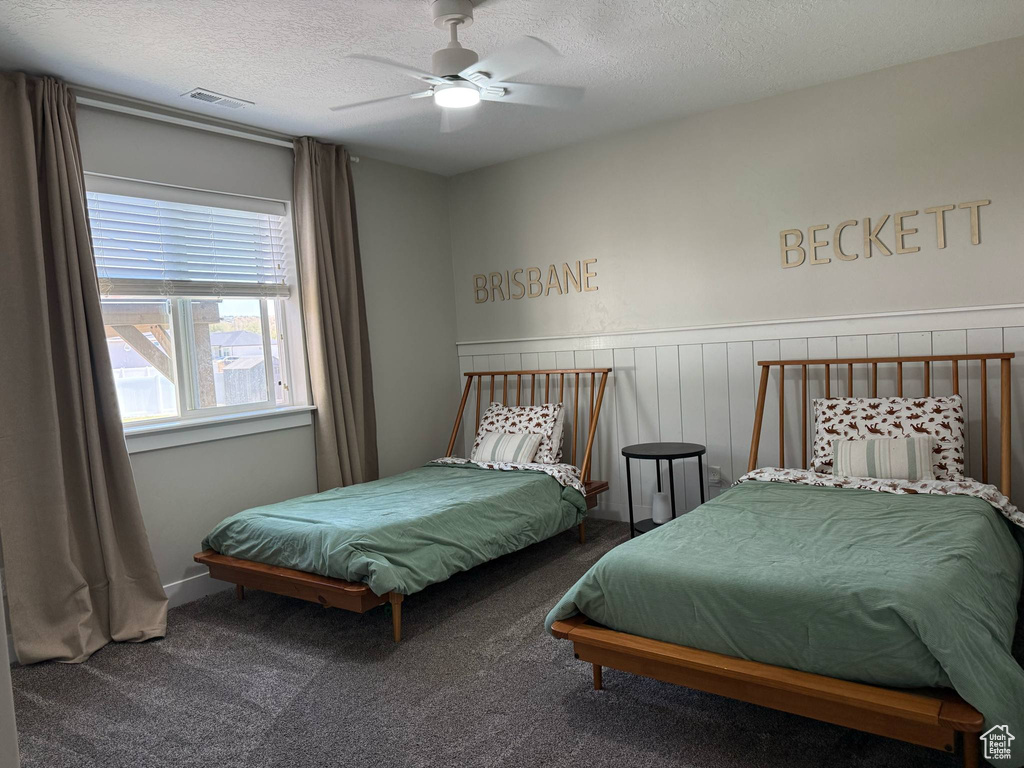 Bedroom with carpet, a textured ceiling, ceiling fan, and wainscoting