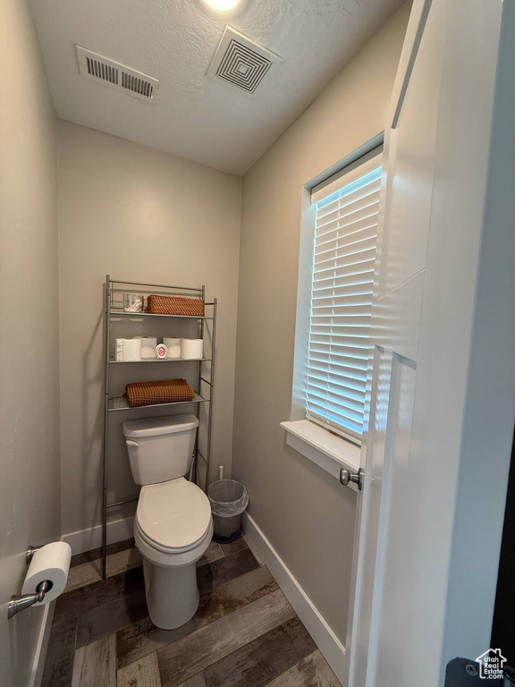 Bathroom featuring toilet, baseboards, wood finished floors, and a textured ceiling