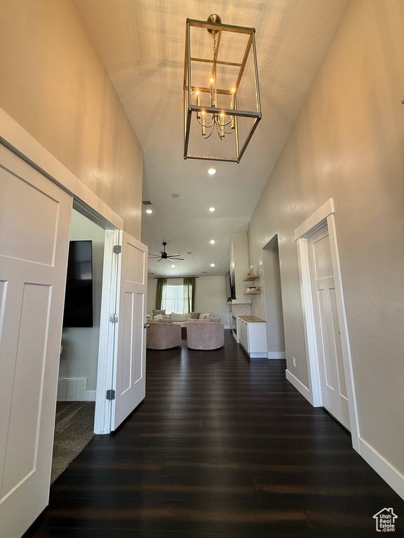 Living room featuring dark wood-style floors, baseboards, a chandelier, a ceiling fan, and high vaulted ceiling