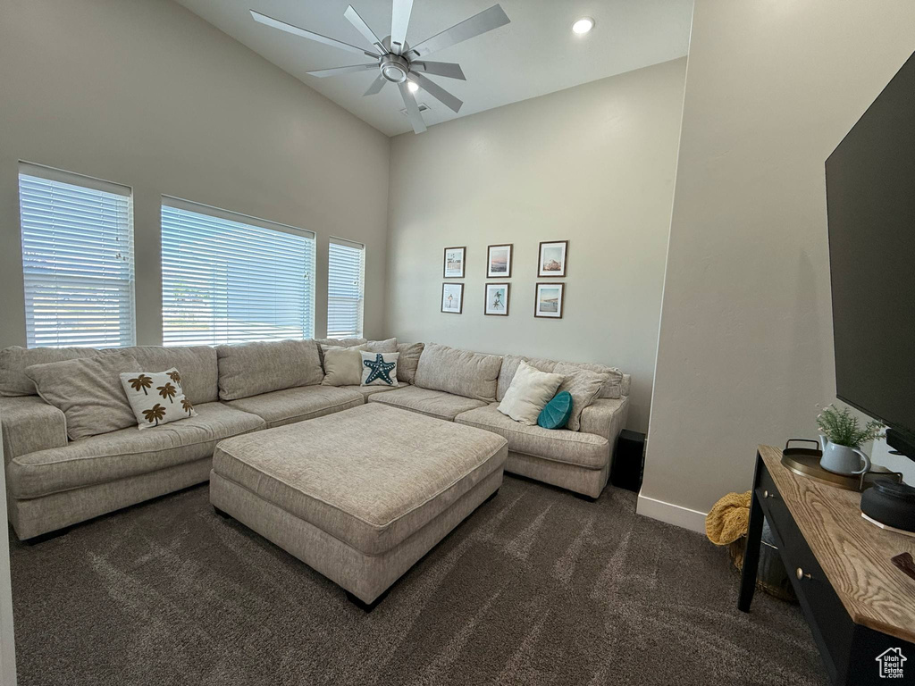 Living area featuring dark colored carpet, ceiling fan, baseboards, and high vaulted ceiling