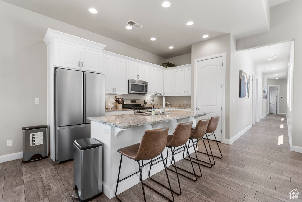 Kitchen featuring stainless steel appliances, a sink, white cabinets, light stone counters, and recessed lighting