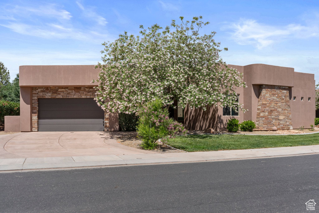 Pueblo revival-style home featuring stucco siding, a garage, stone siding, and concrete driveway