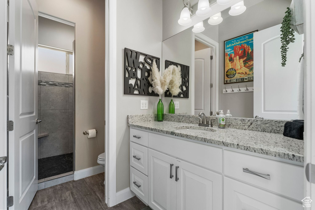 Full bathroom with toilet, vanity, tiled shower, wood finished floors, and baseboards