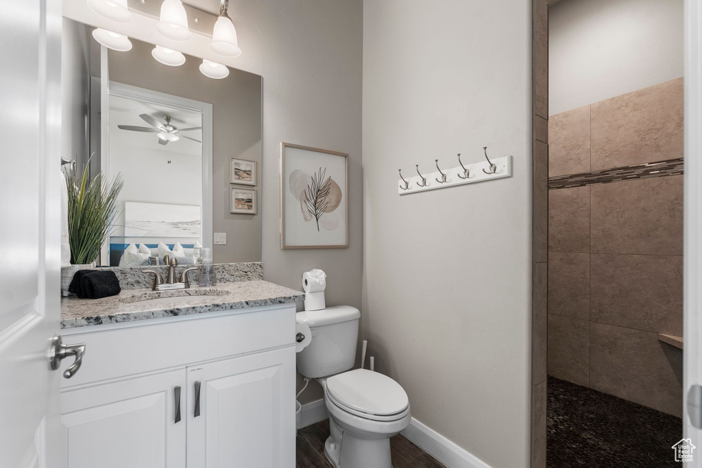 Bathroom featuring a ceiling fan, toilet, vanity, ensuite bath, and tiled shower