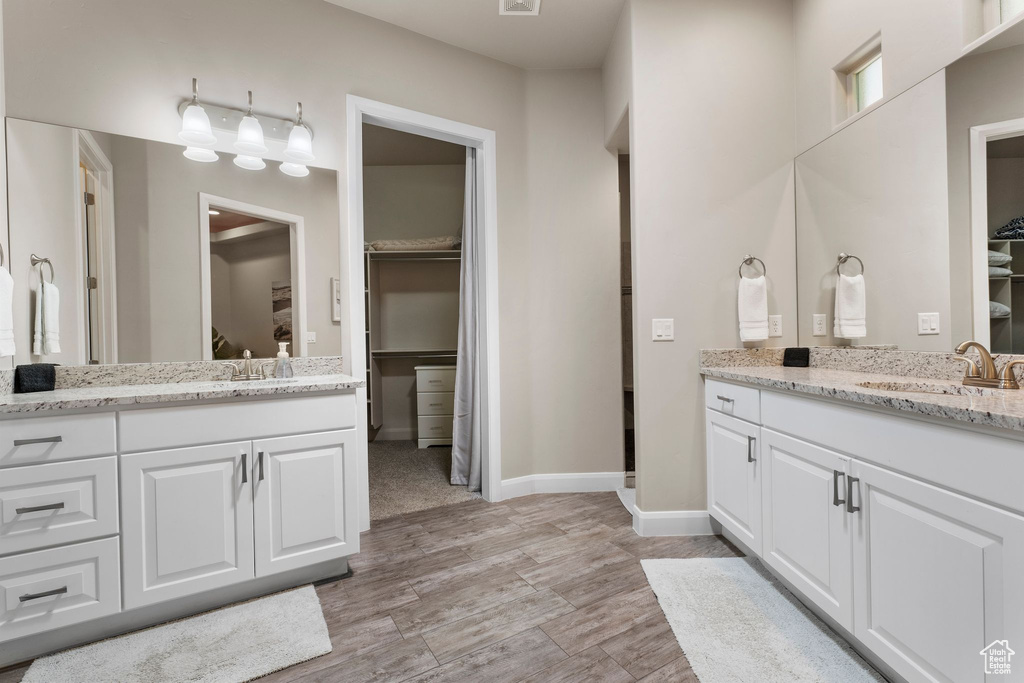 Full bath featuring two vanities, a walk in closet, baseboards, and wood finished floors