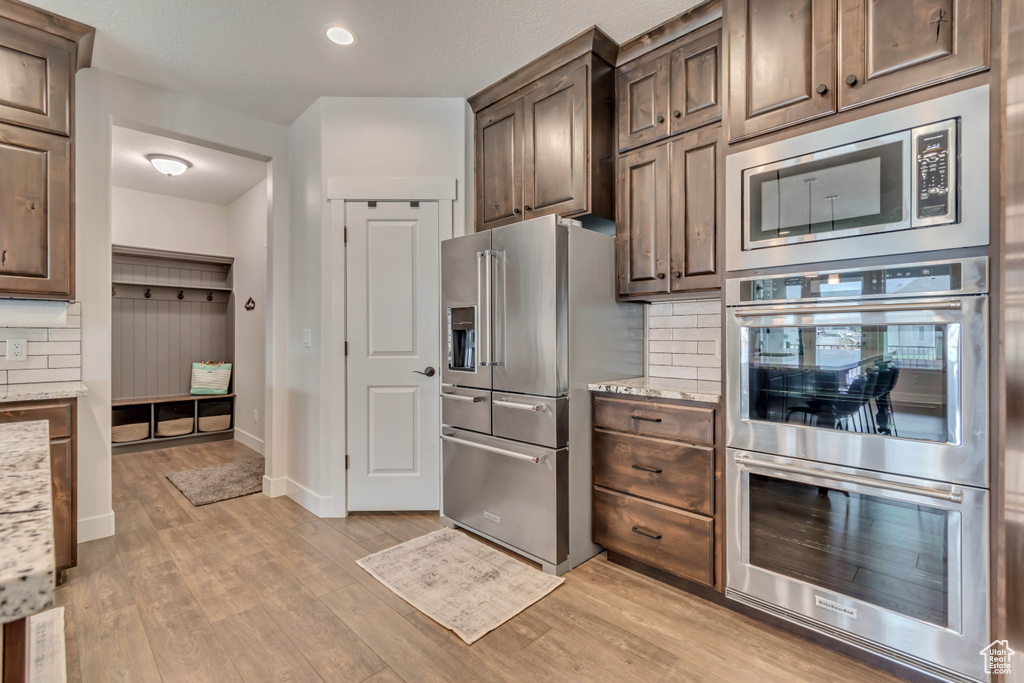 Kitchen with stainless steel appliances, decorative backsplash, light wood-type flooring, light stone counters, and baseboards