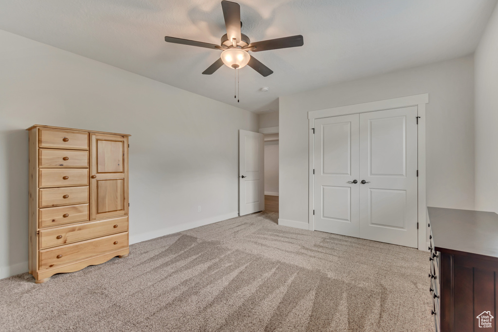 Unfurnished bedroom with light colored carpet, baseboards, a closet, and a ceiling fan