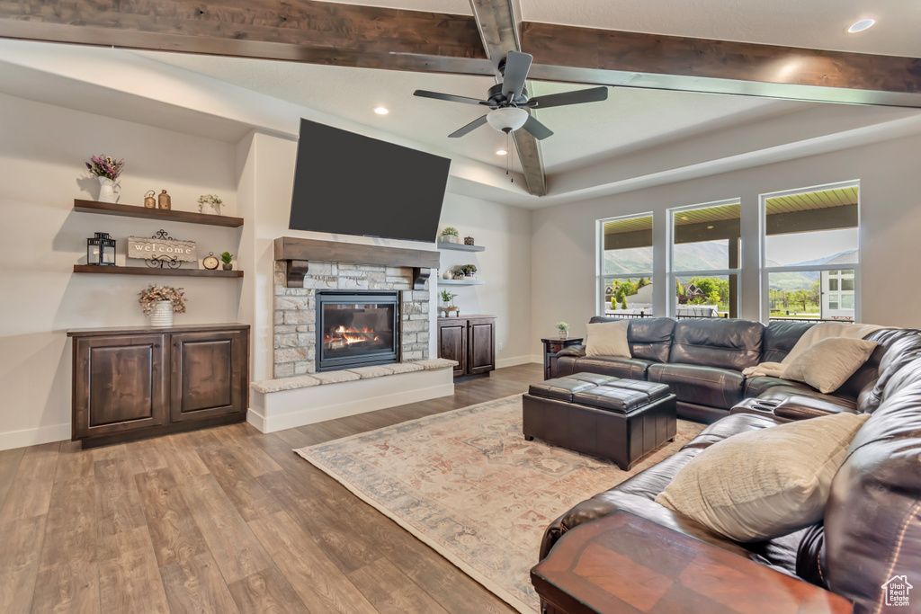 Living room with recessed lighting, a ceiling fan, wood finished floors, beam ceiling, and a stone fireplace