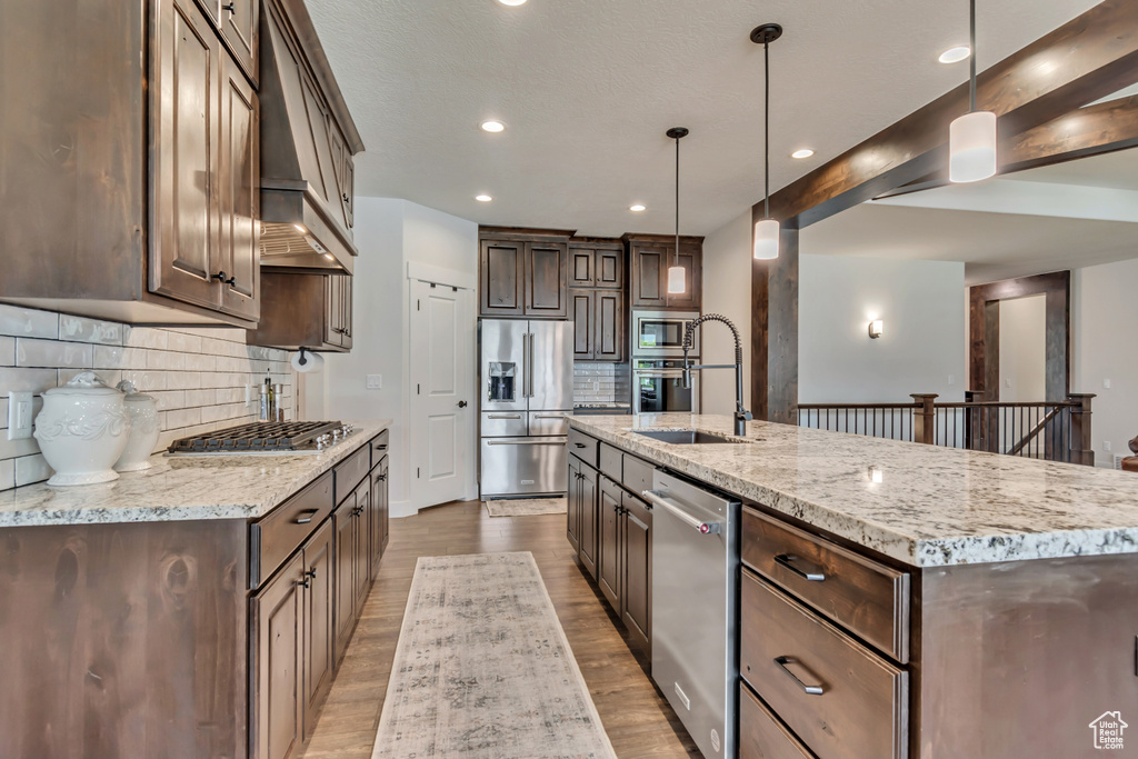 Kitchen featuring appliances with stainless steel finishes, a sink, dark brown cabinetry, decorative backsplash, and custom exhaust hood