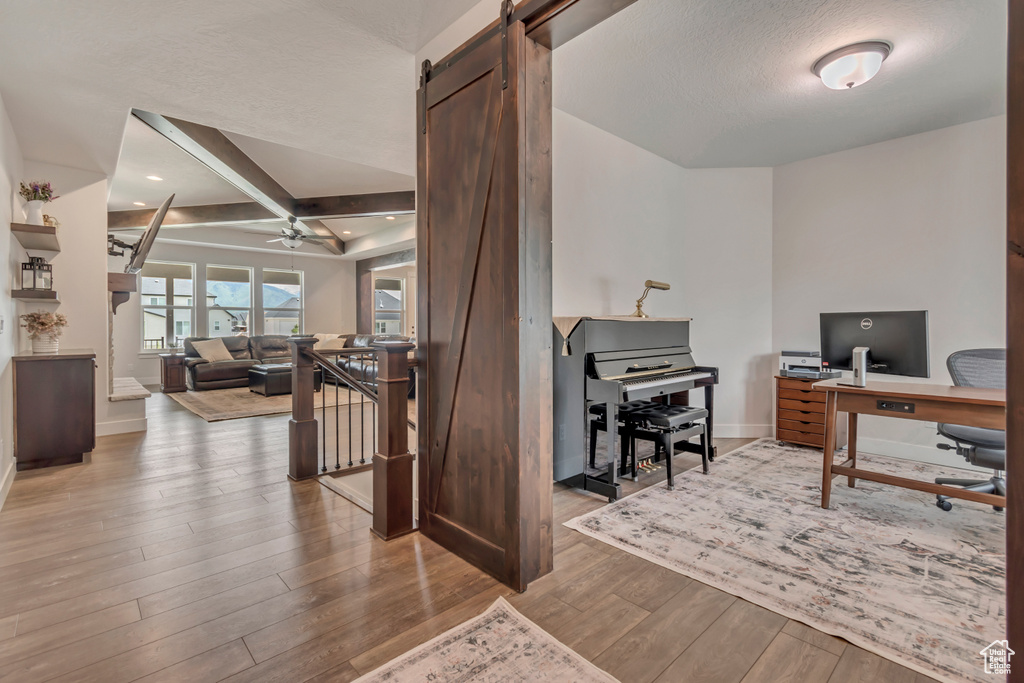 Office area with wood finished floors, baseboards, a ceiling fan, beam ceiling, and a barn door