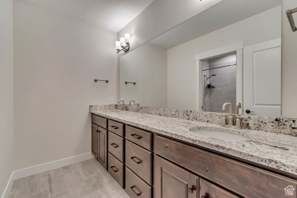 Bathroom featuring baseboards, a tile shower, and double vanity
