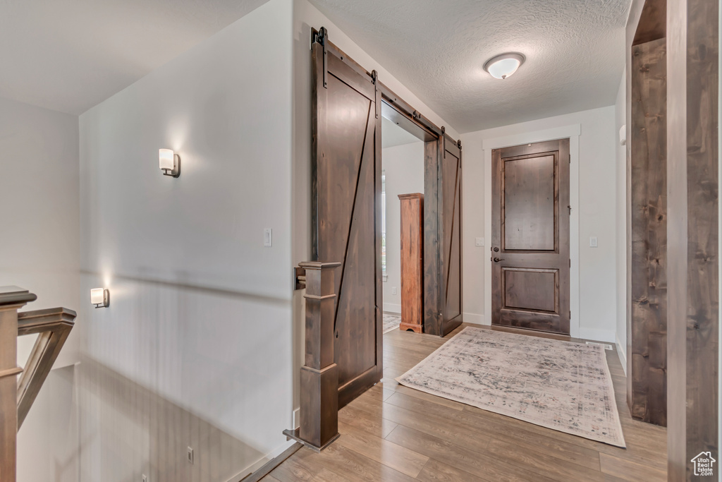 Foyer entrance featuring a barn door, light wood-style floors, baseboards, and a textured ceiling