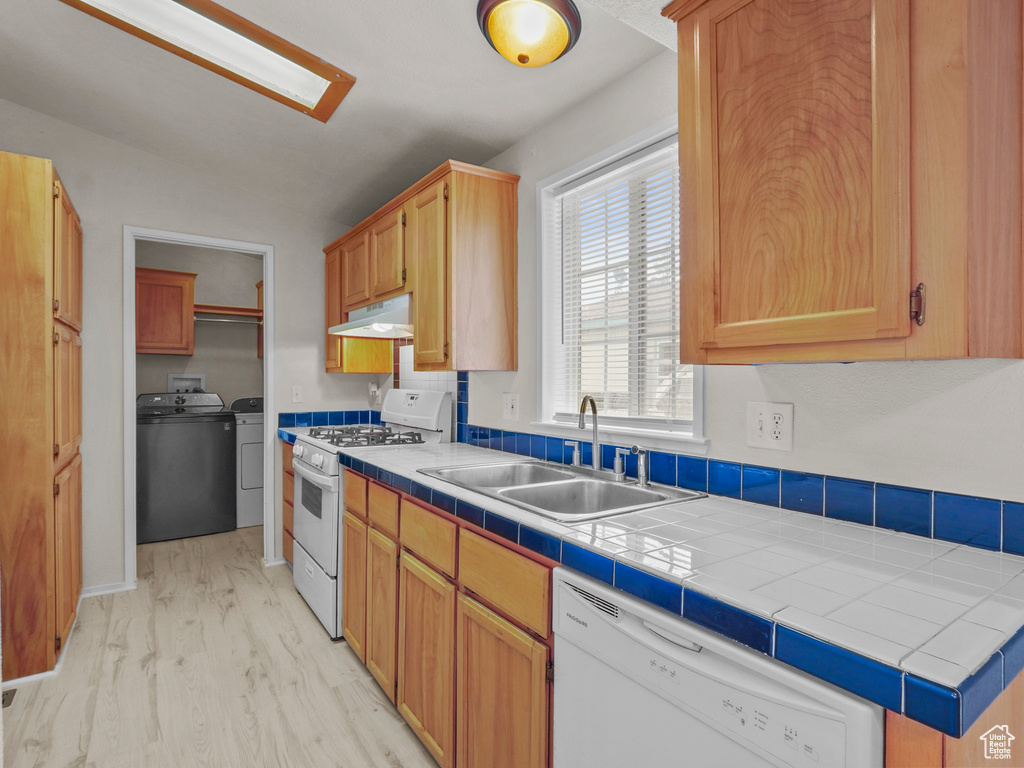 Kitchen with white appliances, a sink, under cabinet range hood, washing machine and clothes dryer, and light wood finished floors