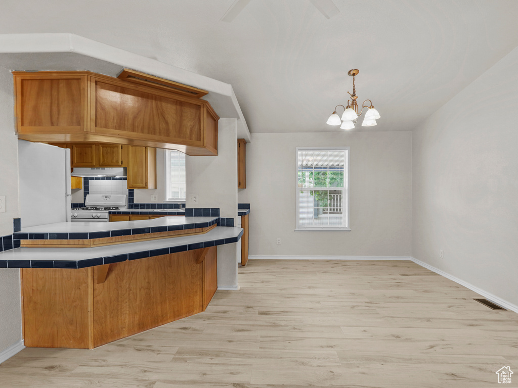 Kitchen featuring tile countertops, light wood-style floors, under cabinet range hood, a chandelier, and baseboards