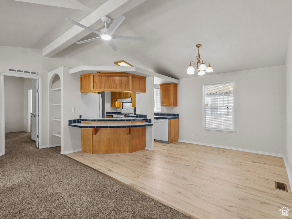 Kitchen featuring tile counters, a peninsula, a breakfast bar area, a chandelier, and white appliances