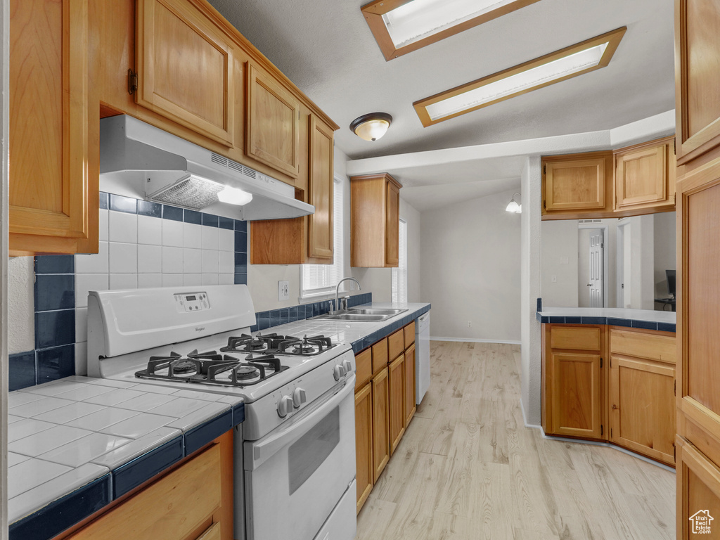 Kitchen featuring white appliances, under cabinet range hood, a sink, and tile countertops