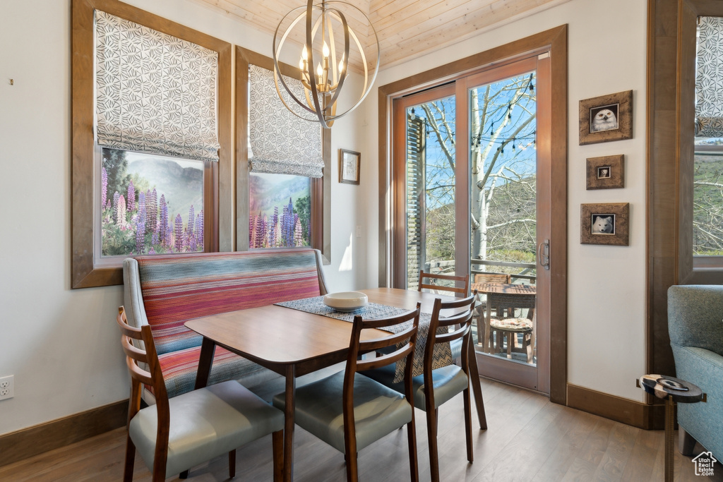 Dining room featuring baseboards, light wood-style flooring, wooden ceiling, a chandelier, and healthy amount of natural light