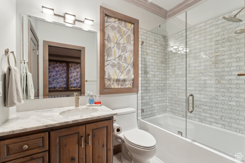 Bathroom featuring vanity, shower / bath combination with glass door, toilet, and ornamental molding