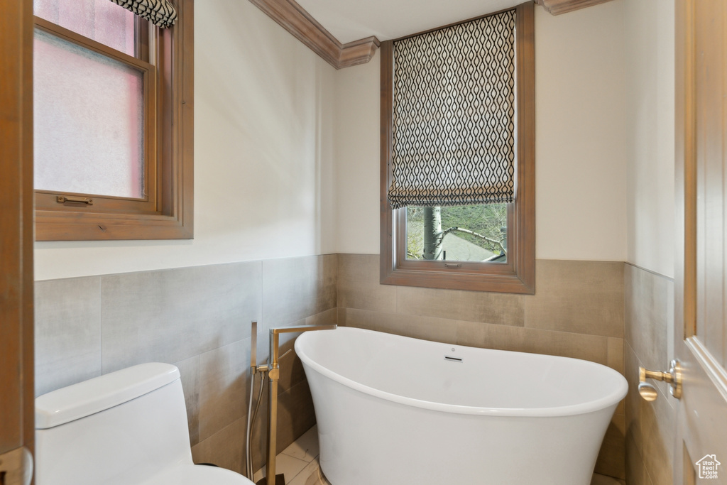 Full bathroom featuring tile walls, toilet, a soaking tub, a wainscoted wall, and crown molding