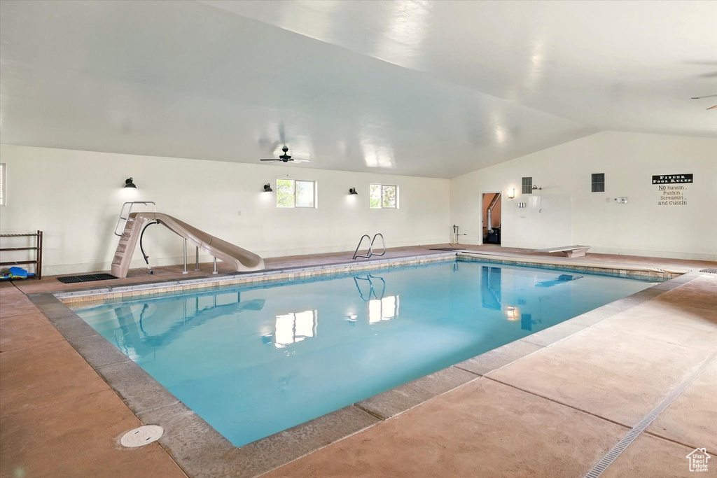 Indoor pool featuring a water slide, a ceiling fan, and a diving board
